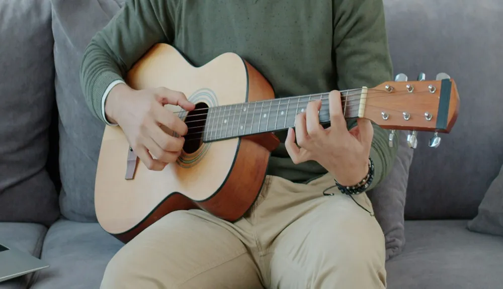 Close-up of someone practicing acoustic guitar on a sofa